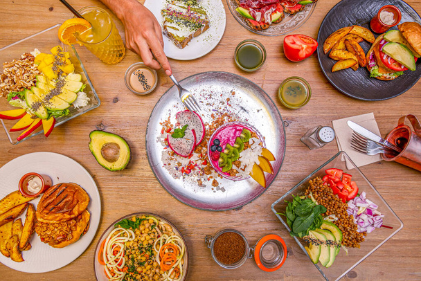 Bonito conjunto de alimentos saludables, veganos, ensaladas y postres con una mano sosteniendo un tenedor - Foto, imagen