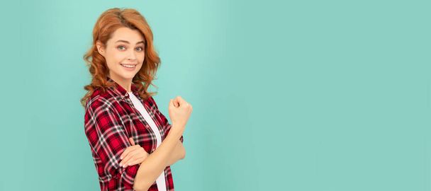 happy redhead woman in checkered shirt threatening with fist on blue background. Woman isolated face portrait, banner with mock up copyspace - Photo, Image
