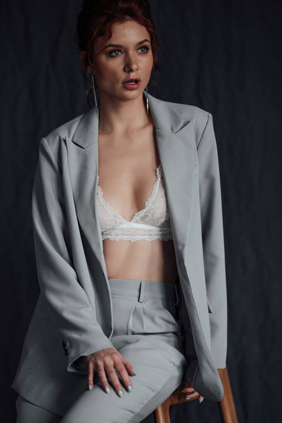Adult beauty elegant young woman in formal evening gray suit with white bra at thoughtful. Stylish ginger curly hair sensual model bare shoulder fashionista posing at studio in fashion pantsuit - Valokuva, kuva