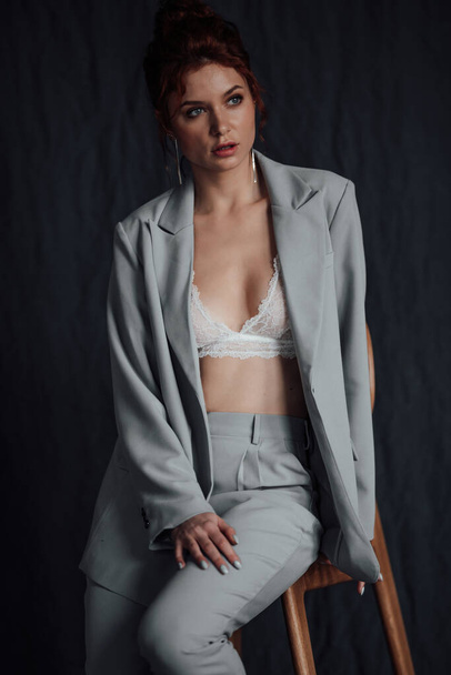 Adult beauty elegant young woman in formal evening gray suit with white bra at thoughtful. Stylish ginger curly hair sensual model bare shoulder fashionista posing at studio in fashion pantsuit - Zdjęcie, obraz