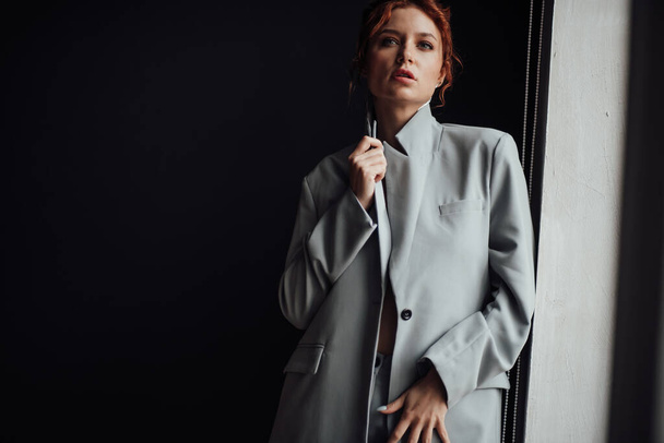 Adult beauty elegant young woman in formal evening gray suit with white bra at thoughtful. Stylish ginger curly hair sensual model bare shoulder fashionista posing at studio in fashion pantsuit - Foto, Bild