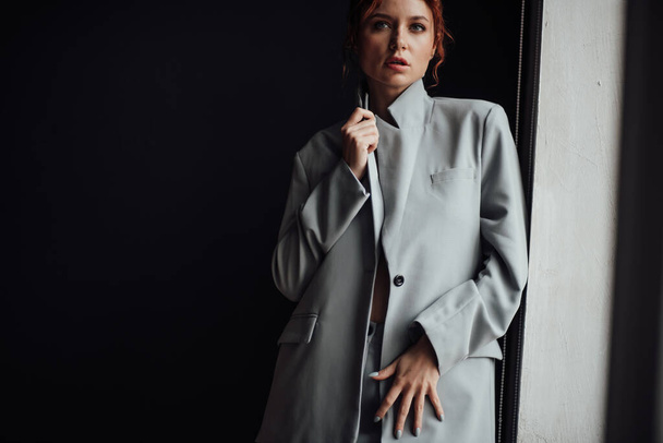 Adult beauty elegant young woman in formal evening gray suit with white bra at thoughtful. Stylish ginger curly hair sensual model bare shoulder fashionista posing at studio in fashion pantsuit - Φωτογραφία, εικόνα
