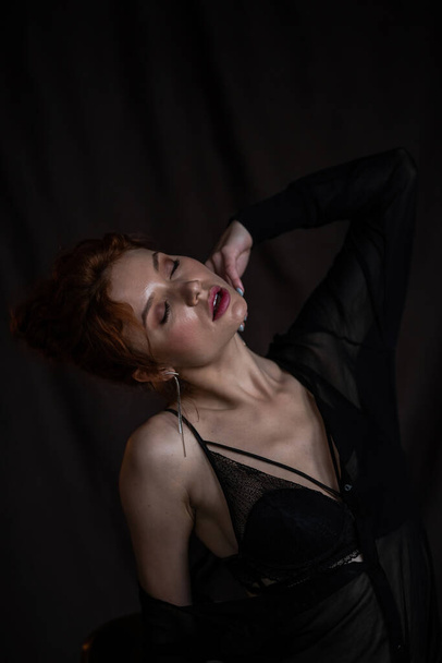 Adult beauty elegant young woman in formal evening black clothing hand on face touching. Stylish ginger curly hair sensual model bare shoulder fashionista posing at studio in fashion pantsuit and bra - Photo, Image
