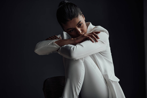 Young adult beauty swarthy woman in formal evening white suit no shirt hand on face touching. Stylish black curly hair sensual african american model fashionista posing at studio in fashion pantsuit - Photo, Image