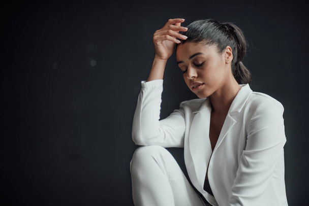Young adult beauty swarthy woman in formal evening white suit no shirt hand on face touching. Stylish black curly hair sensual african american model fashionista posing at studio in fashion pantsuit - Fotografie, Obrázek
