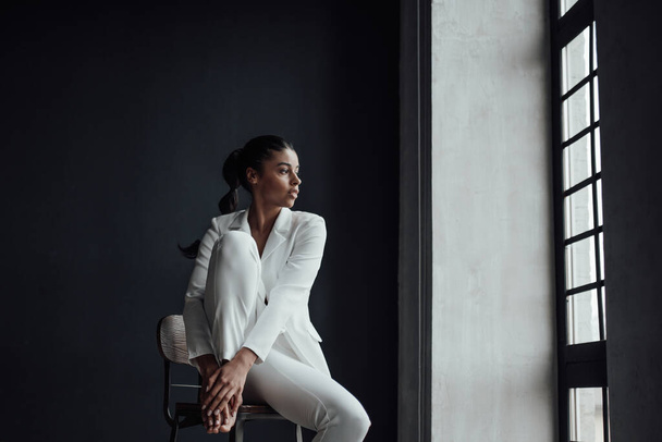 Young adult beauty swarthy woman in formal evening white suit with bra at thoughtful. Stylish black curly hair sensual african american model fashionista posing at studio in fashion pantsuit - Foto, immagini