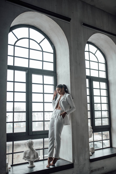 Young adult beauty swarthy woman in formal evening white suit with bra at thoughtful. Stylish black curly hair sensual african american model fashionista posing at studio in fashion pantsuit - Foto, afbeelding