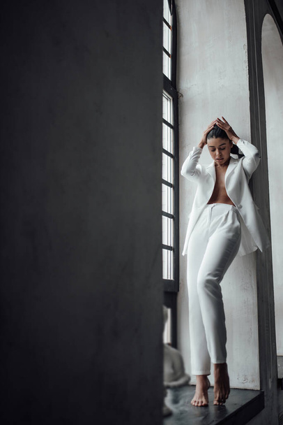 Young adult beauty swarthy woman in formal evening white suit with bra at thoughtful. Stylish black curly hair sensual african american model fashionista posing at studio in fashion pantsuit - Photo, Image