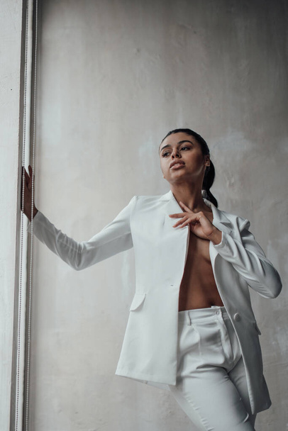 Young adult beauty swarthy woman in formal evening white suit with bra at thoughtful. Stylish black curly hair sensual african american model fashionista posing at studio in fashion pantsuit - Foto, Bild