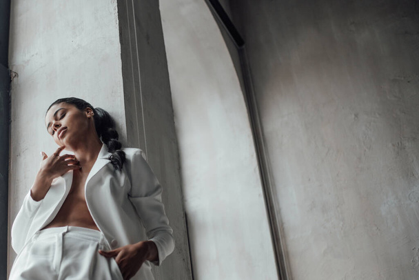 Young adult beauty swarthy woman in formal evening white suit with bra at thoughtful. Stylish black curly hair sensual african american model fashionista posing at studio in fashion pantsuit - Fotografie, Obrázek