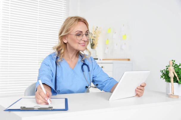 Doctor with glasses and tablet consulting patient in clinic. Online medicine concept - Foto, imagen