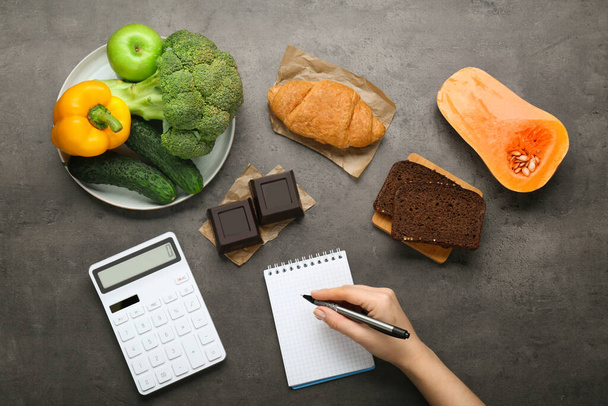 Woman calculating calories at dark grey table with food products, top view. Weight loss concept - Fotó, kép