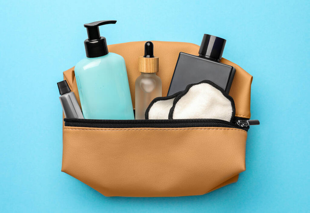 Preparation for spa. Compact toiletry bag with different cosmetic products on light blue background, top view - Photo, Image