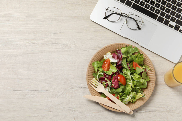Fresh vegetable salad, glass of juice and laptop on white wooden table at workplace, flat lay with space for text. Business lunch - Fotoğraf, Görsel