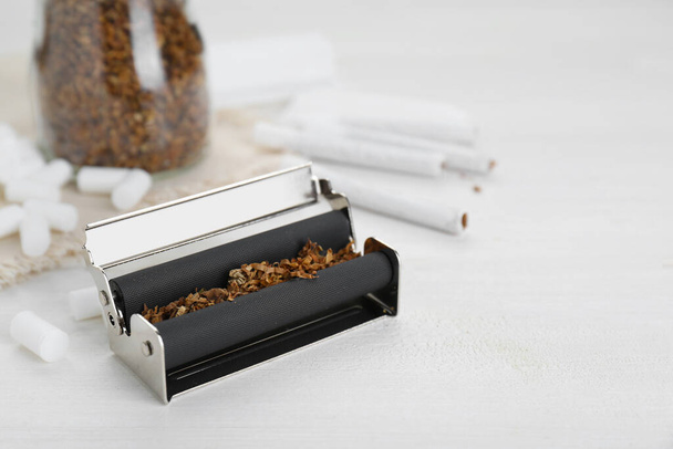 Roller with tobacco on white wooden table, space for text. Making hand rolled cigarettes - Photo, image