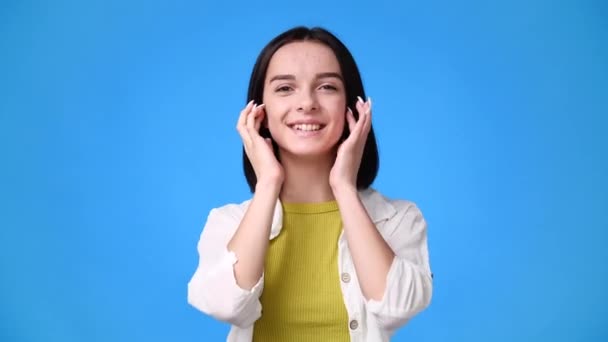 4k Video von einem Mädchen fixiert ihre Haare und lächelt süß über blauen Hintergrund. Konzept der Emotionen. - Filmmaterial, Video