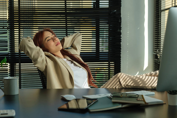 Mujer de negocios pacífica apoyada en una cómoda silla de oficina con los ojos cerrados - Foto, imagen