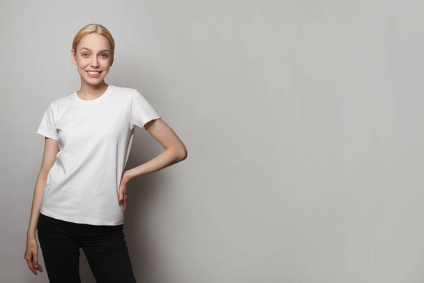 Fiatal nő fehér üres üres póló áll szemben szürke stúdió fal banner háttér - Fotó, kép
