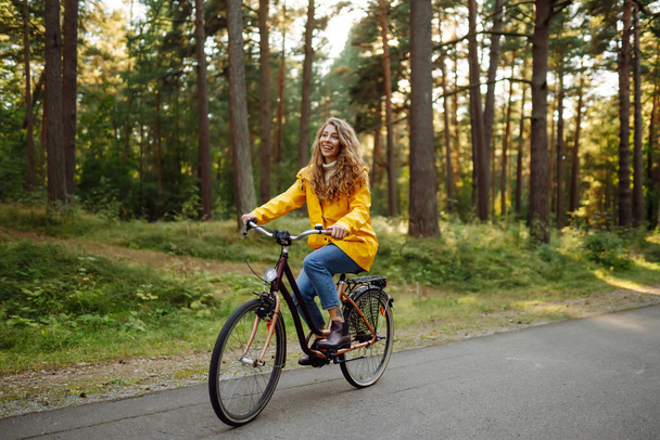 Young woman in yellow coat riding bicycle park. Active day.  - Fotó, kép
