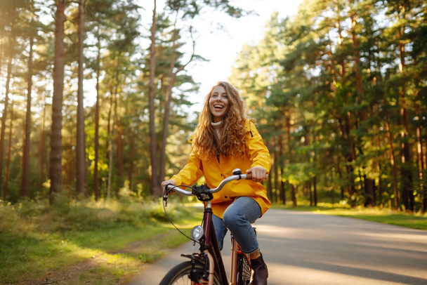 Young woman in yellow coat riding bicycle park. Active day.  - Fotoğraf, Görsel