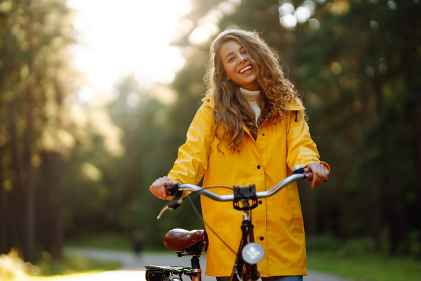 Young woman in yellow coat riding bicycle park. Active day.  - Foto, Imagem