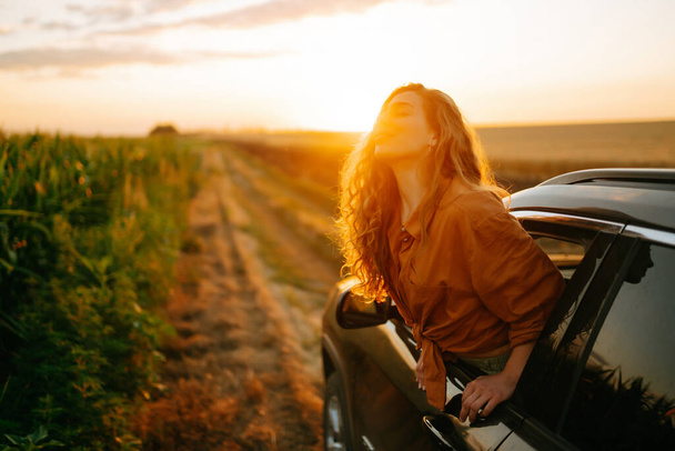 Happy woman outstretches her arms while sticking out the car window. Lifestyle, travel, tourism, nature, active life. - 写真・画像