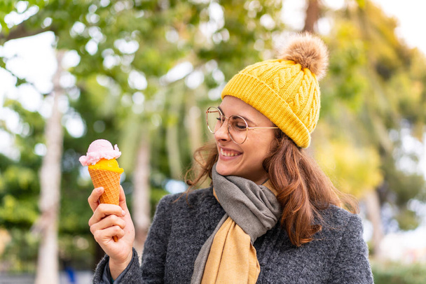Брюнетка с мороженым из корнета на открытом воздухе со счастливым выражением лица - Фото, изображение