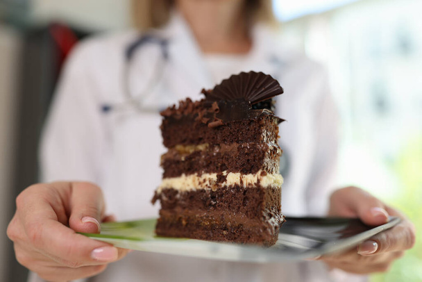 女性食生物学者は不健康な甘い食べ物を避けるように頼む。医者を保持しています大きなスライスのチョコレートケーキ上のプレートで彼女の手を閉じる. - 写真・画像