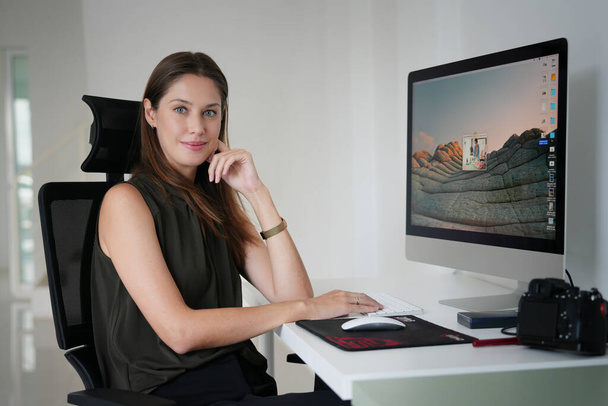 Muotisuunnittelija istuu työpöydän ääressä studiossa katsomassa kannettavaa tietokonetta
 - Valokuva, kuva