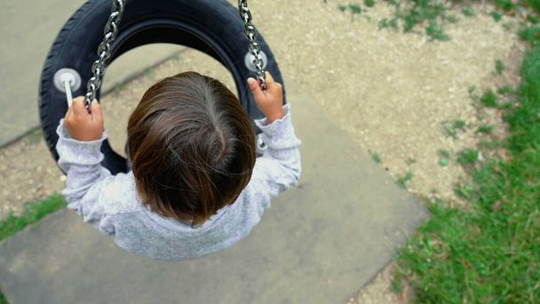 Bambino seduto sull'altalena di pneumatici che gira al parco giochi sognando ad occhi aperti. Vista dall'alto prospettiva di un piccolo ragazzo gira - Foto, immagini