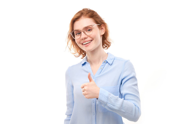 Young redhead woman shows hand with thumbs up and smiles at the camera isolated on white background - Photo, Image
