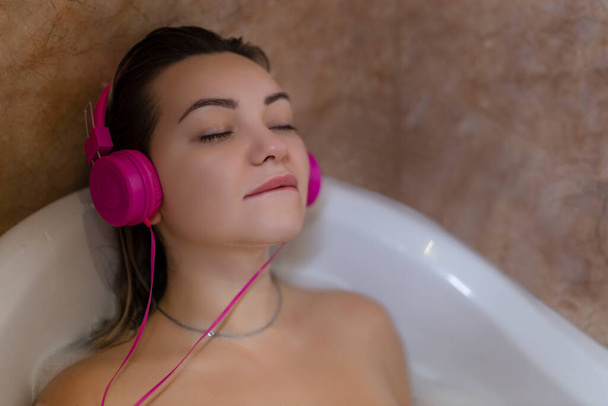 Красивая молодая женщина с наушниками отдыхает в ванной
.  - Фото, изображение