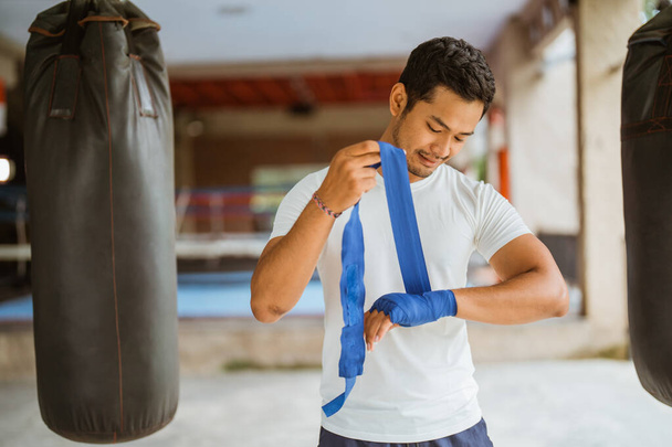 a asian male boxer wearing the boxing wrap gloves while standing with the box ring at the background - Foto, Imagem