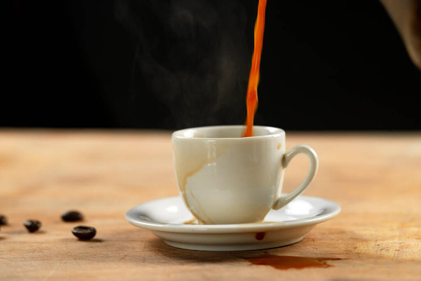 Coffee pouring into a cup on a wooden table. Black background. - Photo, Image