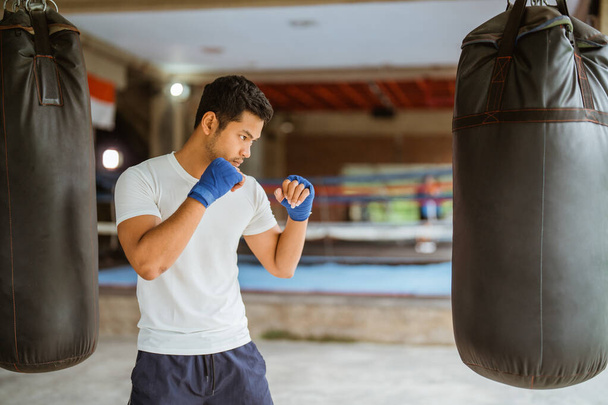 un boxeur frappe sérieusement les sacs lourds au studio de boxe - Photo, image