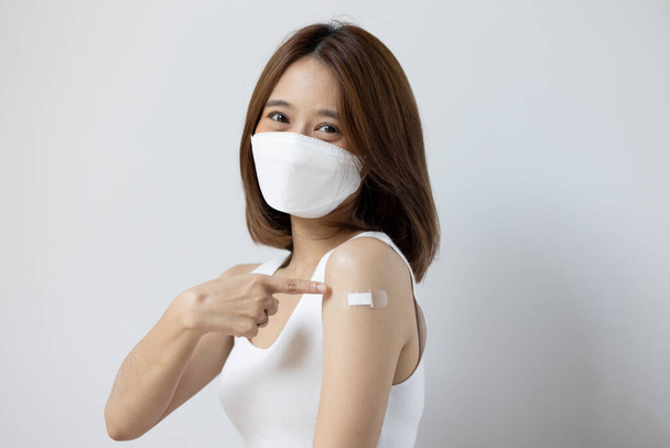 Vakcinovaná asijská mladá žena s obličejovou maskou ukazující na vakcinační obvaz - Fotografie, Obrázek