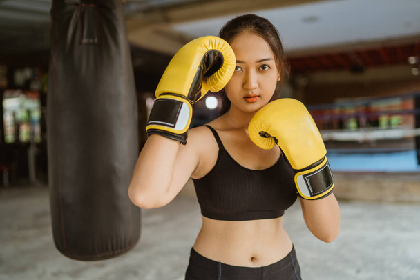 a female boxer standing with the boxing moves at the boxing studio with the box ring at the background - Photo, image