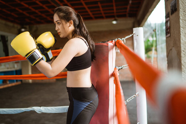 a female boxer standing with punching moves inside the box ring at the boxing studio - Фото, изображение