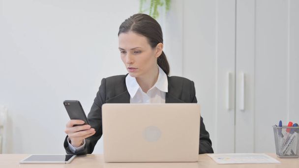 Young Businesswoman using Smartphone while using Laptop - Foto, imagen