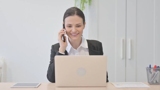 Joven empresaria que habla por teléfono mientras usa el ordenador portátil - Foto, Imagen