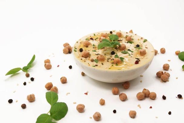 Kompozycja klasycznego hummusa na białym tle w talerzu z ciecierzycy i nasion sezamu, bazylii i przypraw. Projekty kulinarne i spożywcze zdjęcie. Kuchnia wschodnia lub śródziemnomorska - Zdjęcie, obraz