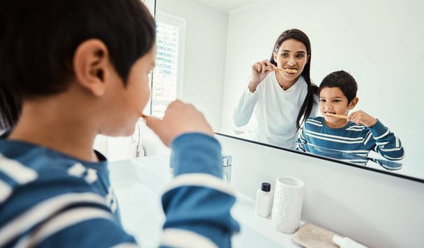 Szczęśliwa rodzina, kobieta i chłopiec w łazience do mycia zębów, opieki zdrowotnej i tworzenia więzi, aby rozpocząć rano w domu. Młody dzieciak, matka i nauczanie ze szczoteczką do zębów, uśmiech i lustro do opieki medycznej. - Zdjęcie, obraz