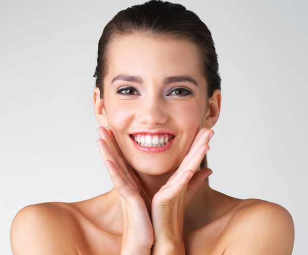 Happy, woman and hands on face in studio for makeup, wellness or cosmetic on grey background. Portrait, smile and girl beauty model with dermatology, satisfaction or luxury routine while isolated. - Φωτογραφία, εικόνα