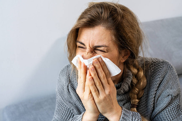 Mujer estornudando en un pañuelo en la sala de estar. Imagen del concepto de Gripe, Medicina y Salud - Foto, Imagen