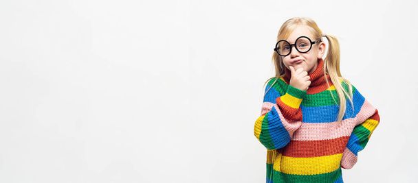 small girl thinking and touching her chin wear rainbow style pullover and hispter glasses isolated on white background, copyspace for your individual text. - Foto, imagen