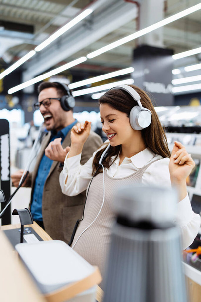 Beautiful and happy middle age couple buying consumer tech products in modern home electronics store. They are choosing high quality hifi audio speakers and audiophiles headphones.  - Foto, Imagen