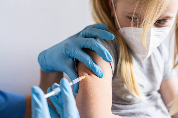 scared blonde child girl looking at the Syringe with vaccine for covid-19 coronavirus, flu, dangerous infectious from a doctor. While being vaccinated or receiving a shot at vaccination center. - Φωτογραφία, εικόνα