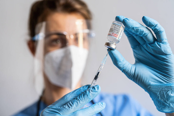 BERLIN, NÉMETORSZÁG DECEMBER 10 2021: Egy női egészségügyi dolgozó a vakcinázási központban elhelyezett Moderna Covid-19 vakcinát tartalmazó injekciós üvegből vesz le egy adagot. - Fotó, kép