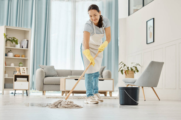 Woman cleaning the floor with a mop in the living room in home with a smile. Happy asian cleaner doing housework or job in a clean lounge, hotel room or house while smiling and alone spring cleaning. - Photo, Image