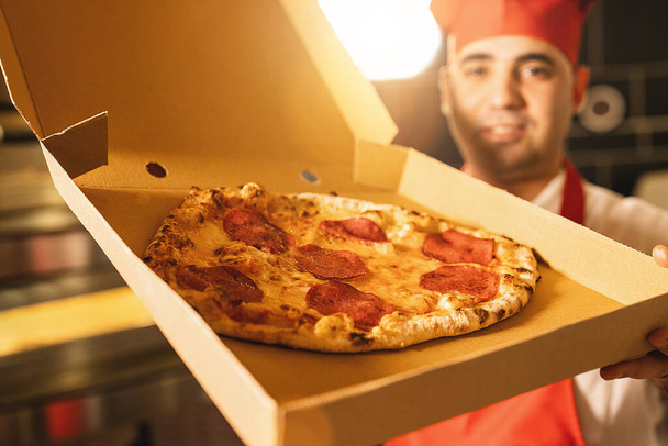 felice pizzaiolo italiano che tiene la pizza di salame in una scatola per la consegna alla pizzeria italiana - Foto, immagini